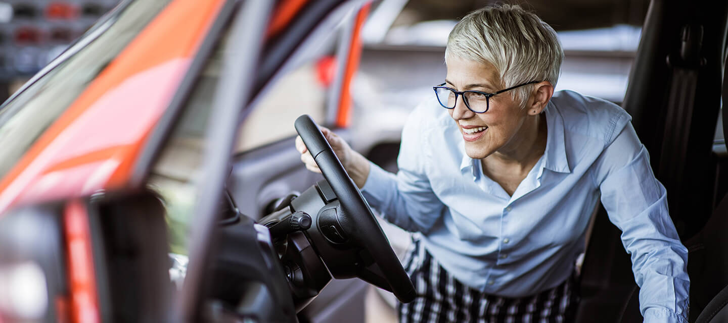 Happy mature woman buying a car in a showroom.