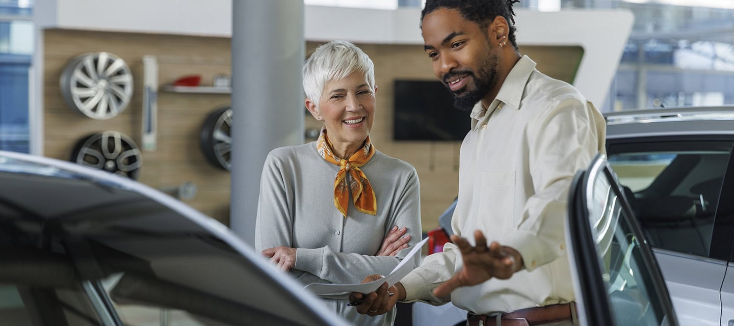 Happy salesperson showing car to customer in showroom