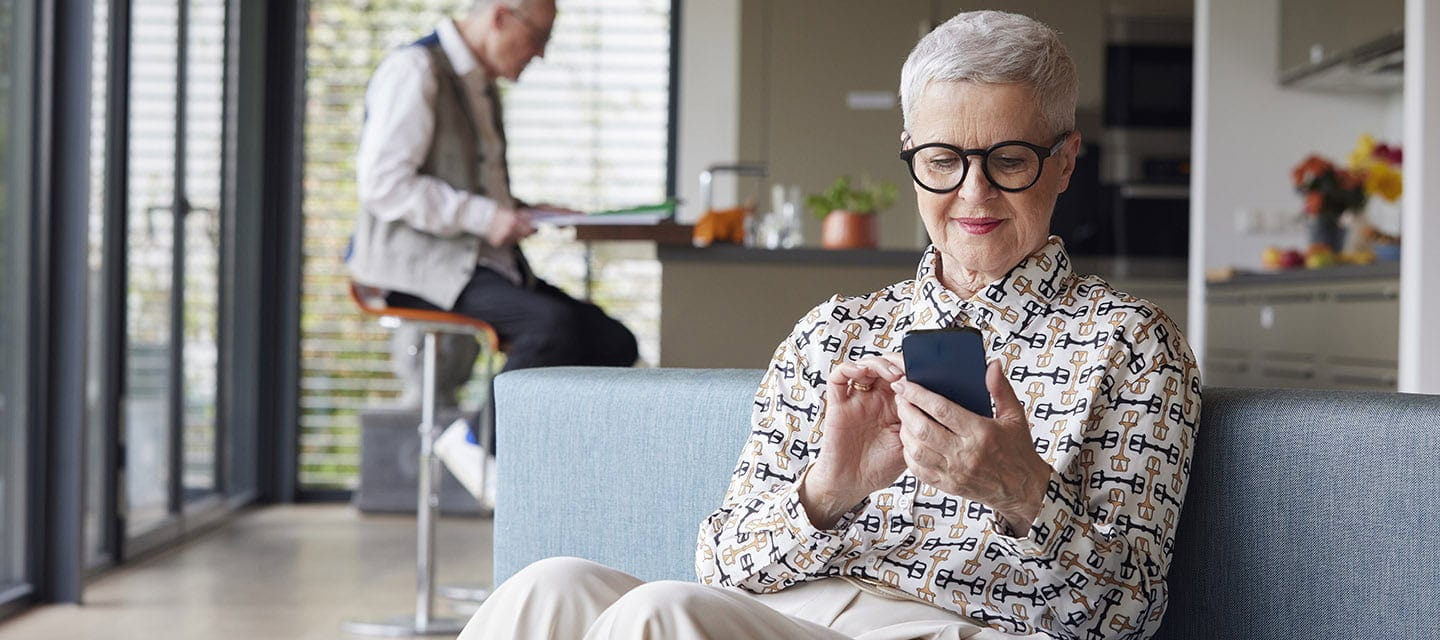 Senior woman sitting on couch at home using mobile phone