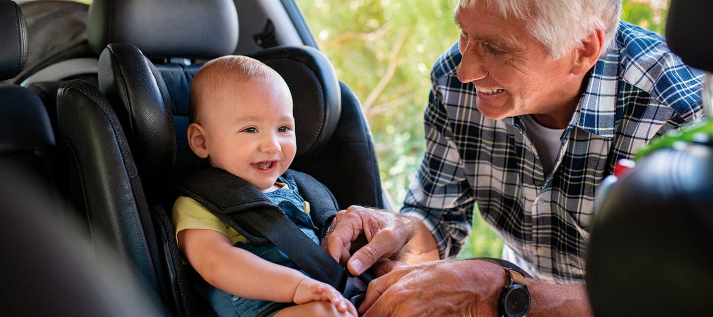 A grandparent plugging their grandchild in to a child car seat