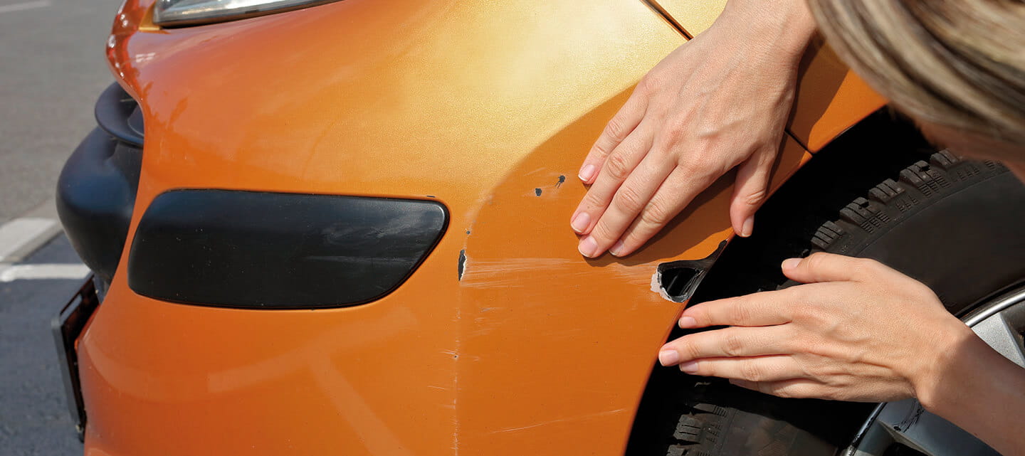 A woman checking a big scratch and dent in her car