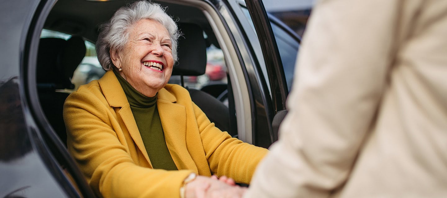 Senior lady getting out of the car, caregiver helping her, holding her hands.