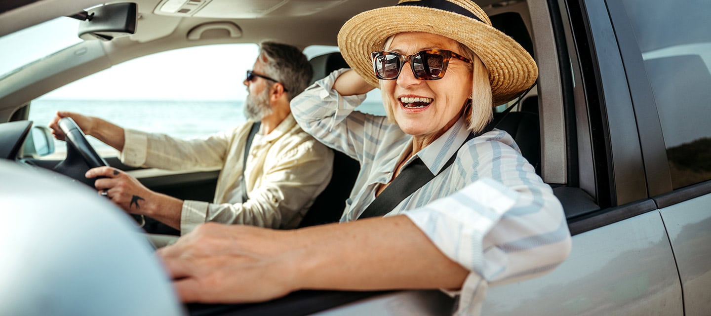 Senior woman leaning through car window while enjoying ride with her husband.