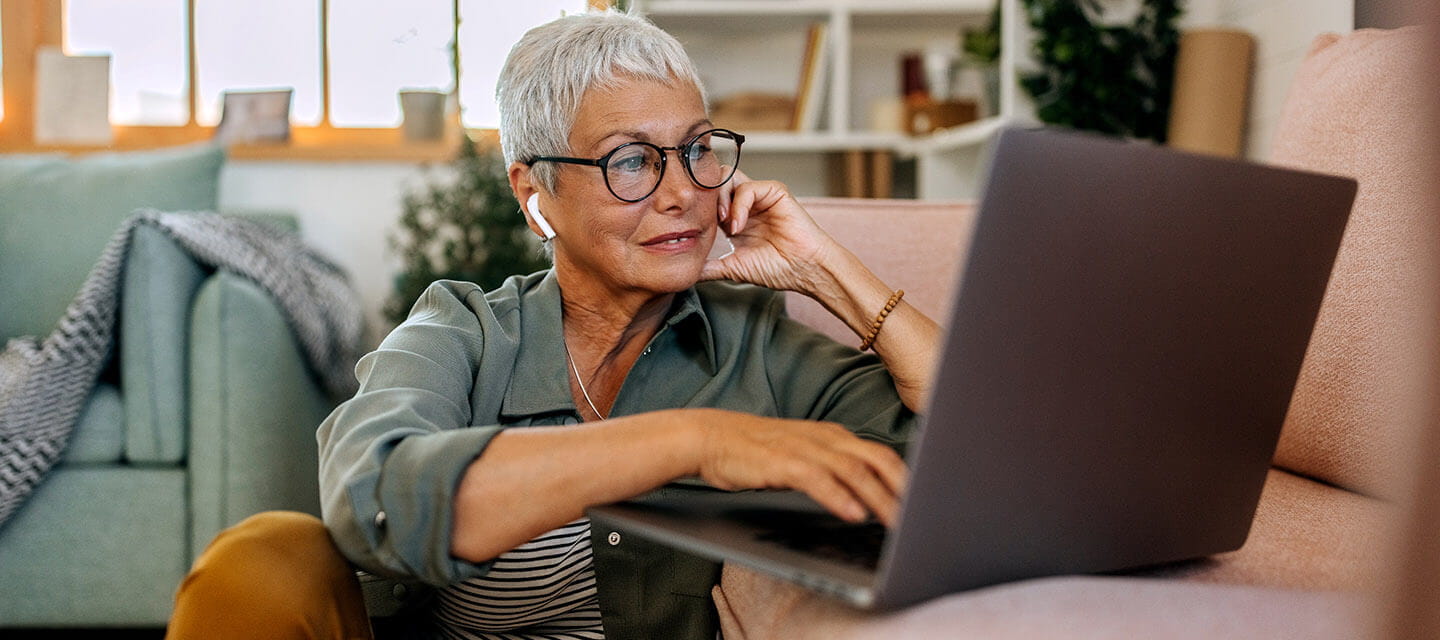 Mature woman using laptop on living room floor with wireless headphones