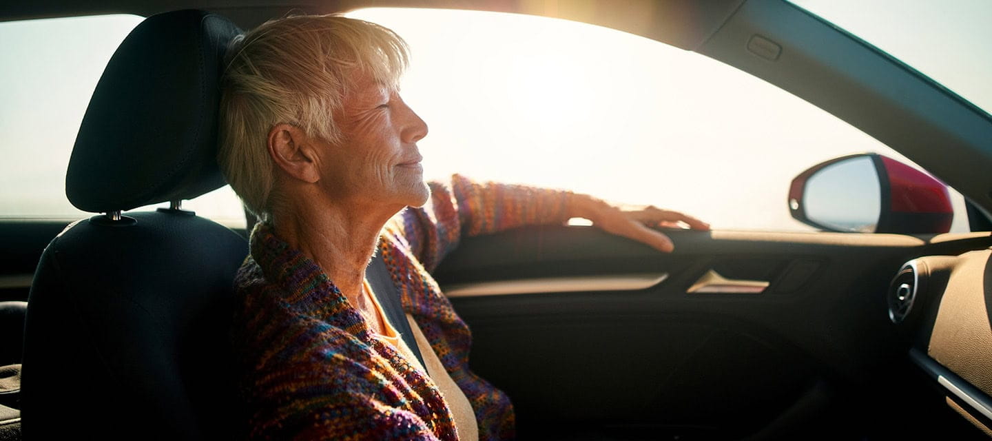 A mature woman sitting in her car on a very sunny day