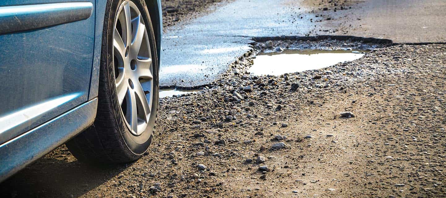 Car parked near a big pothole on an empty road