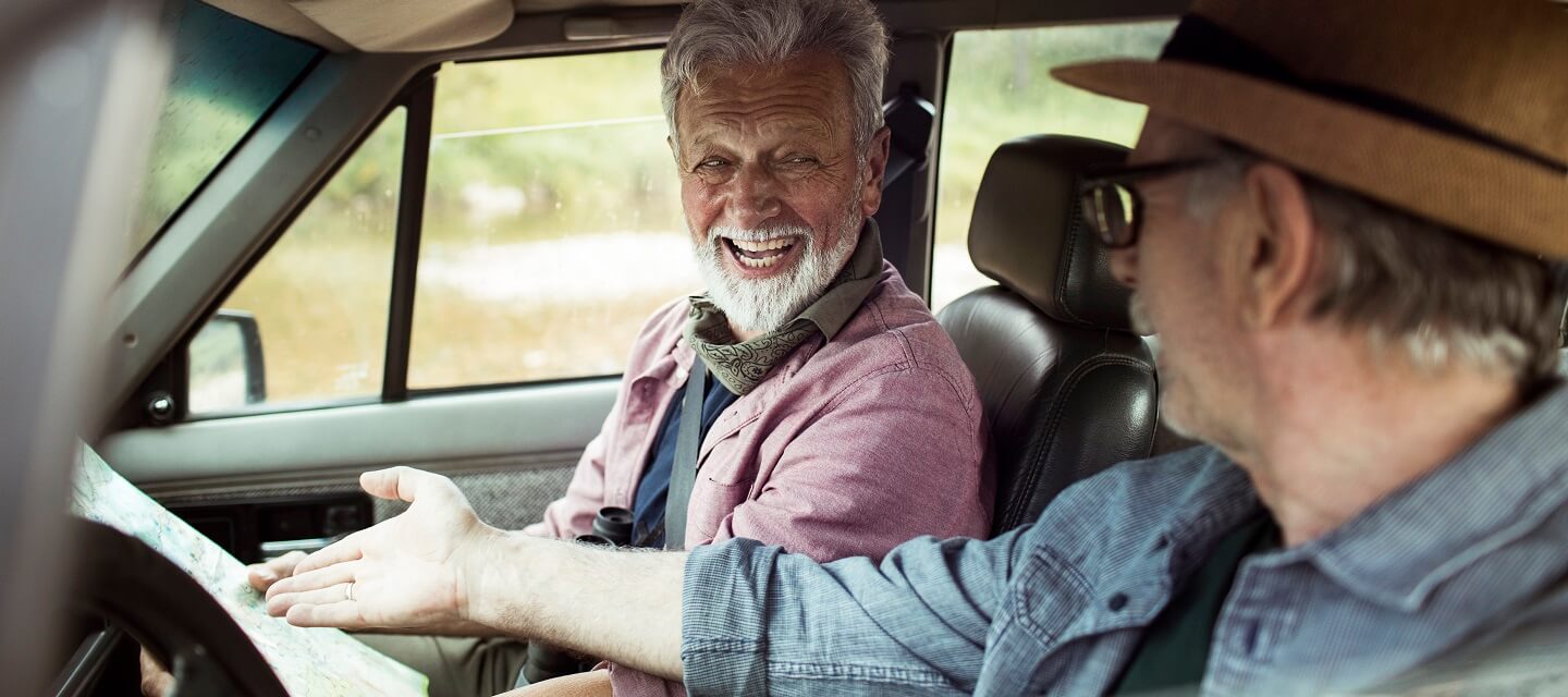 Two men laughing while reading a map in their car