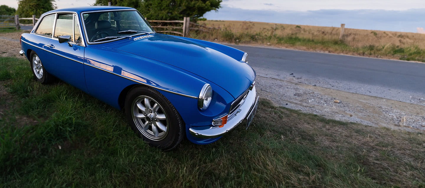A bright blue British classic car, is parked up off road.