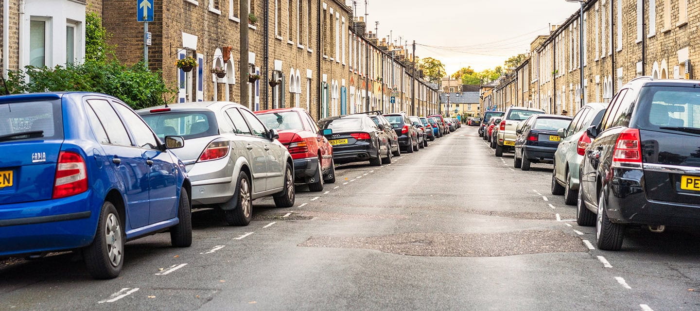 A long street of traditional terraced houses with cars parked on the road in Cambridge.