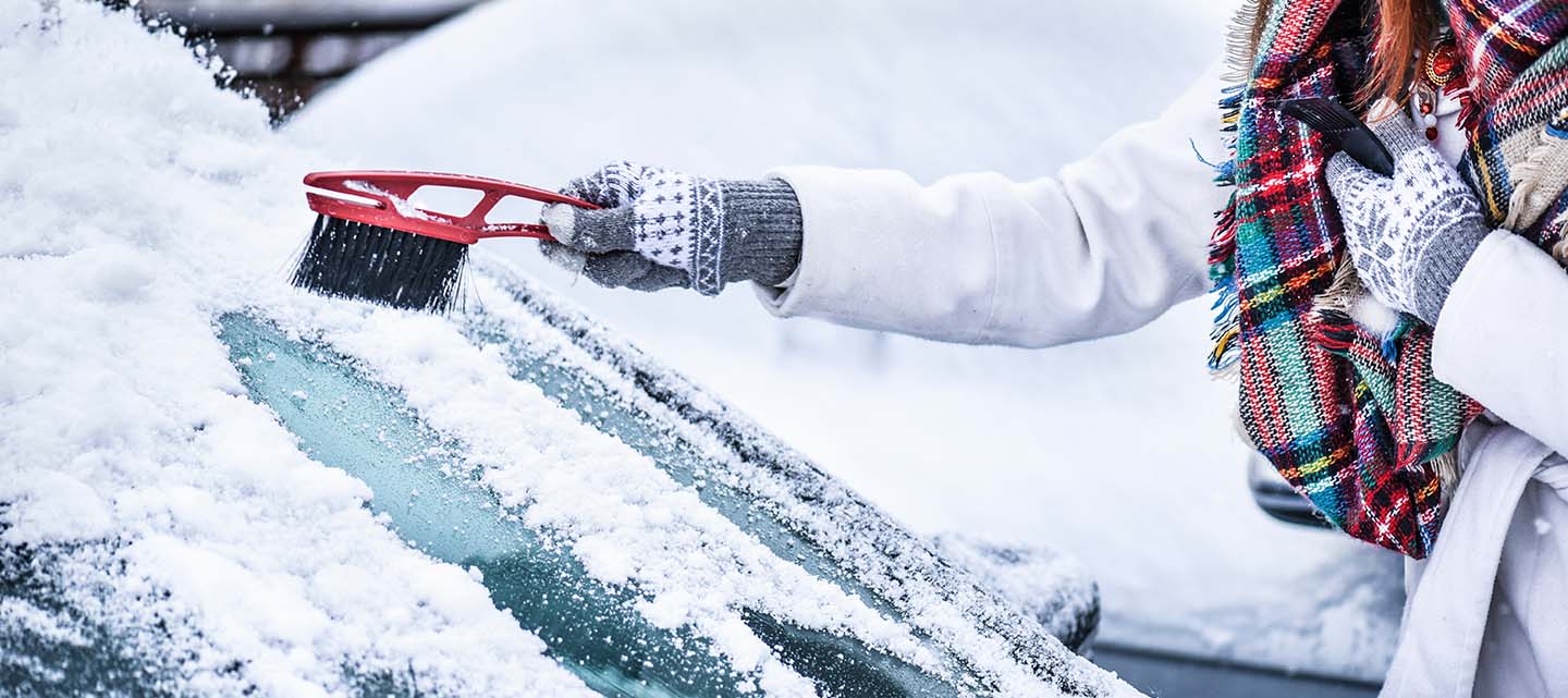 A woman scraping snow and ice from their car windscreen