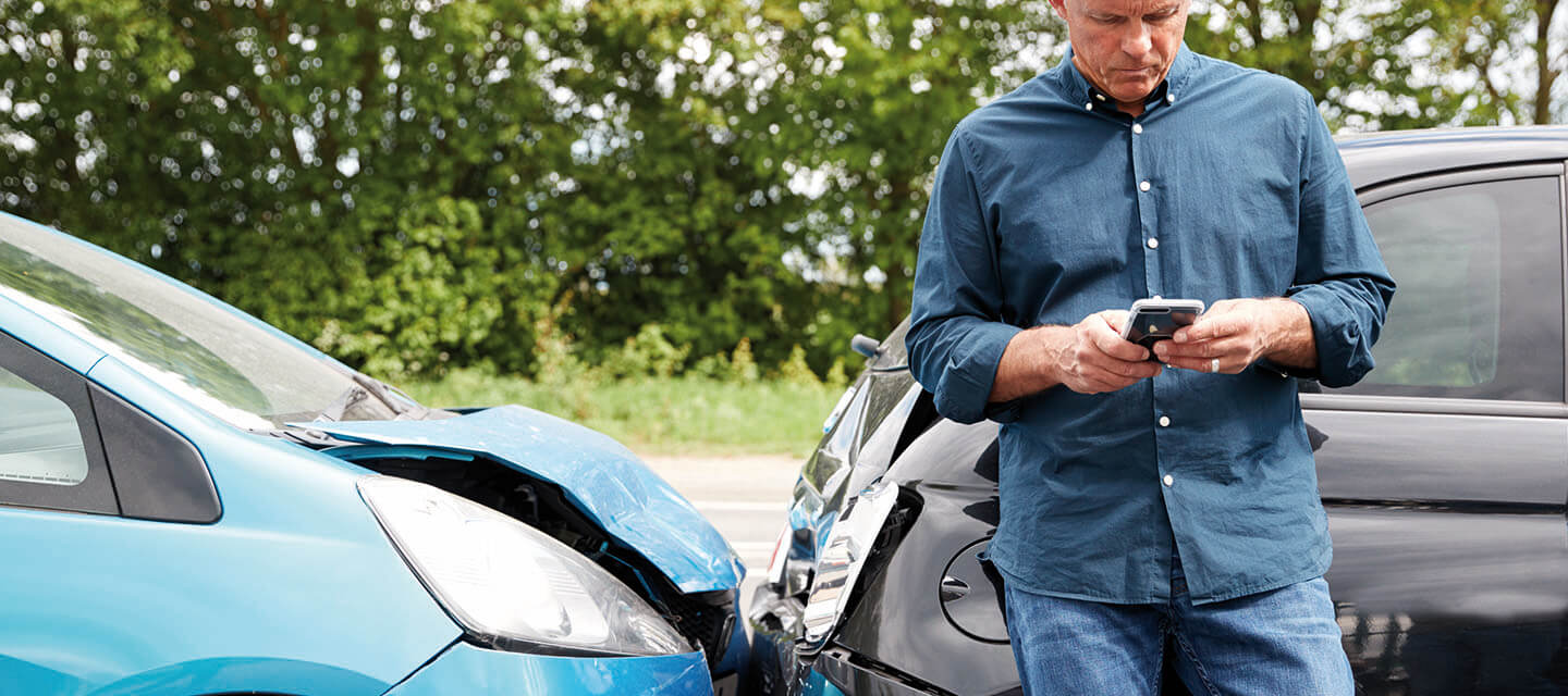 A man standing by 2 cars that have crashed