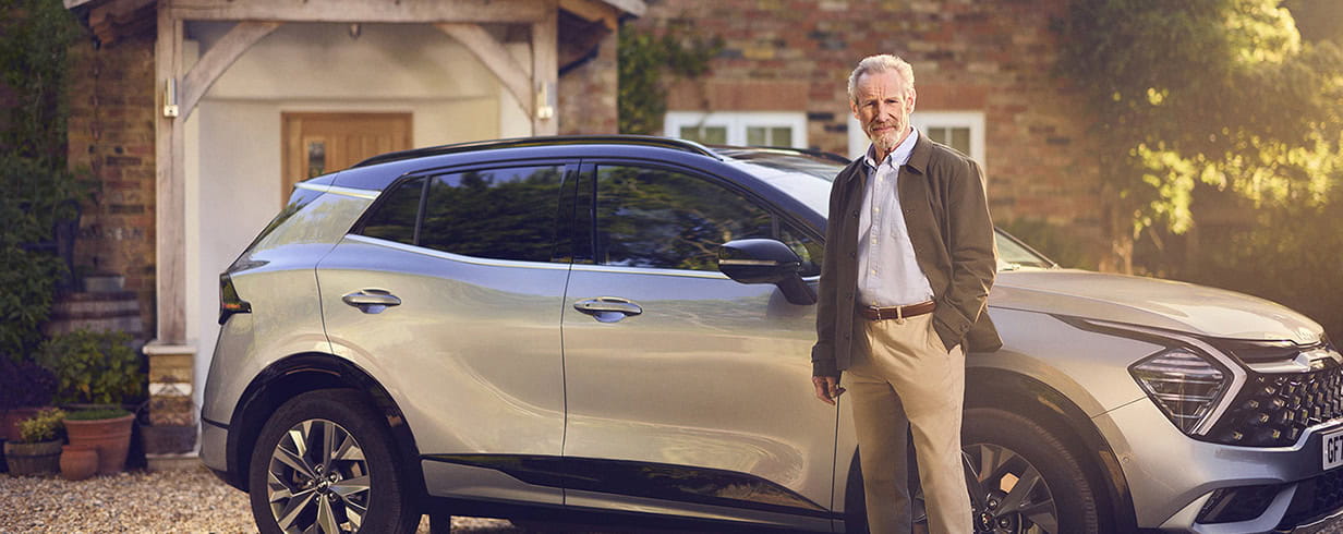 A mature man standing confidently in front of his car parked on his driveway.