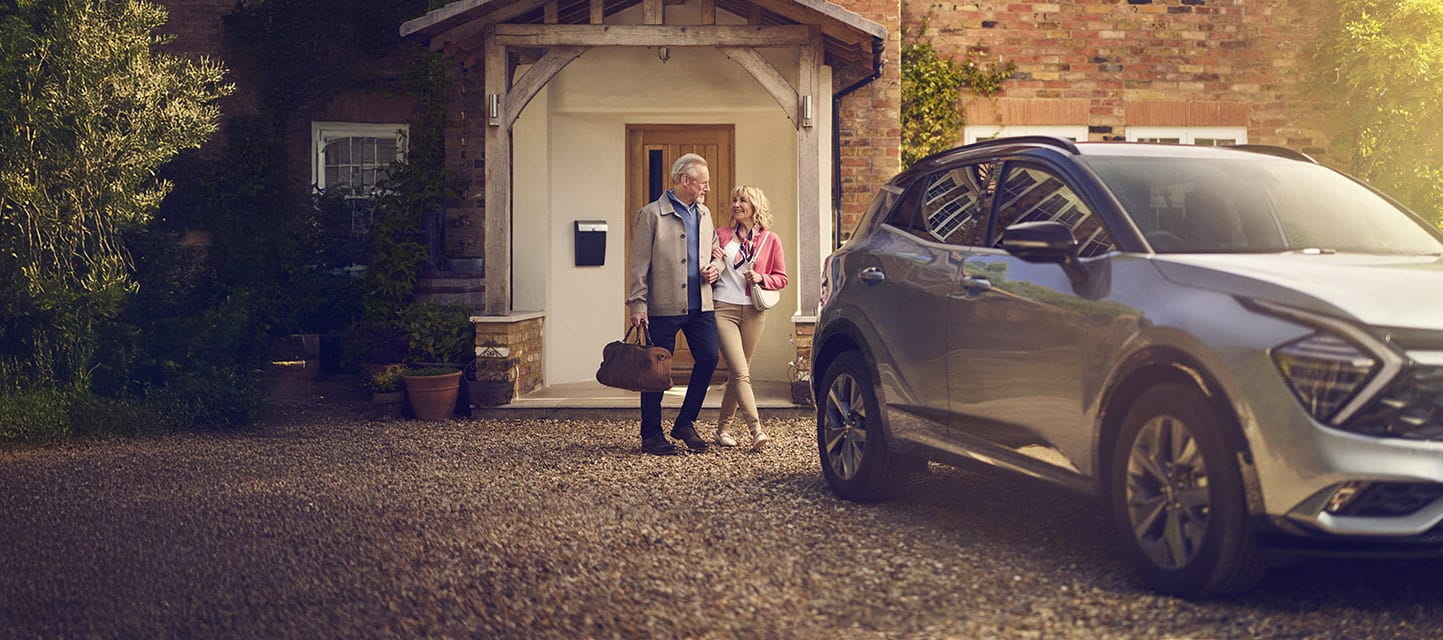 A happy mature couple walking arm in arm from their front door to their car, which is parked on their driveway.