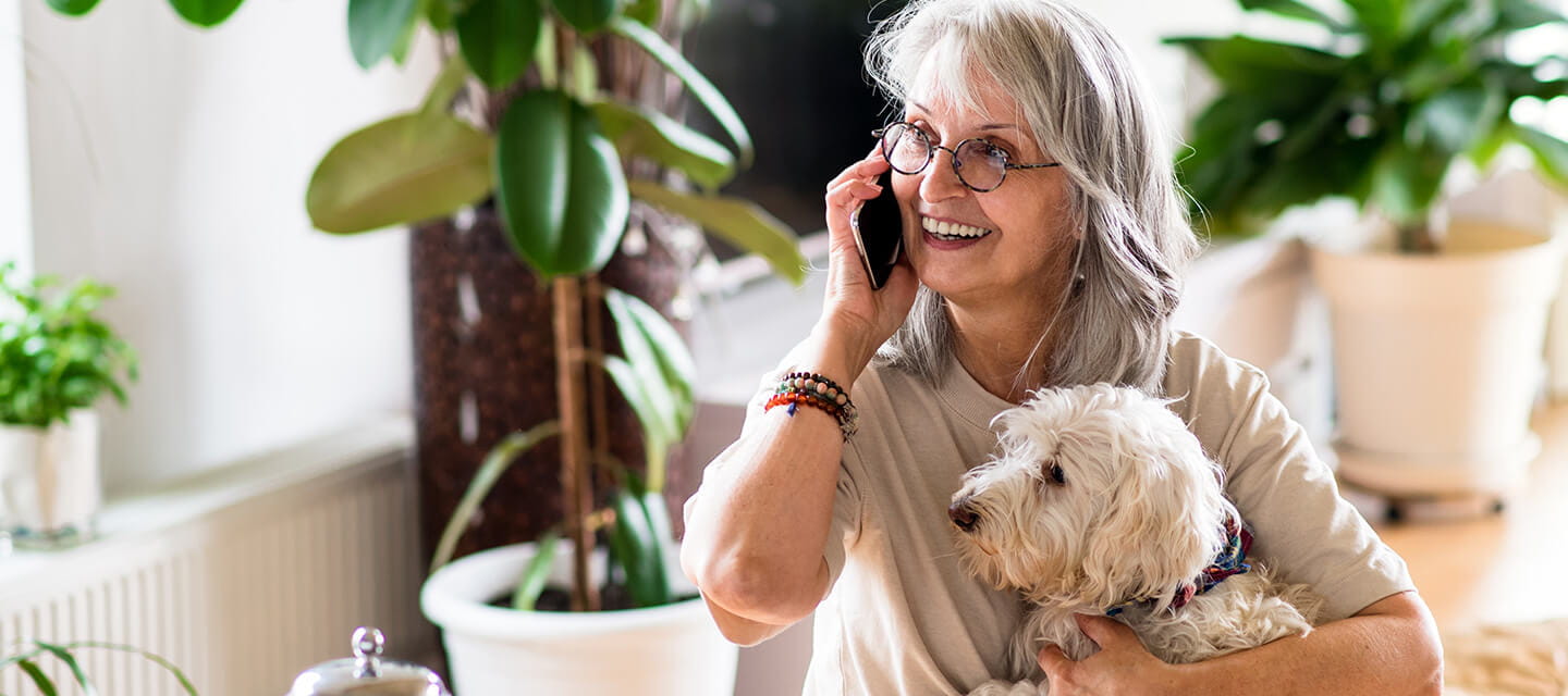 A mature woman on the phone smiling while holding her pet dog