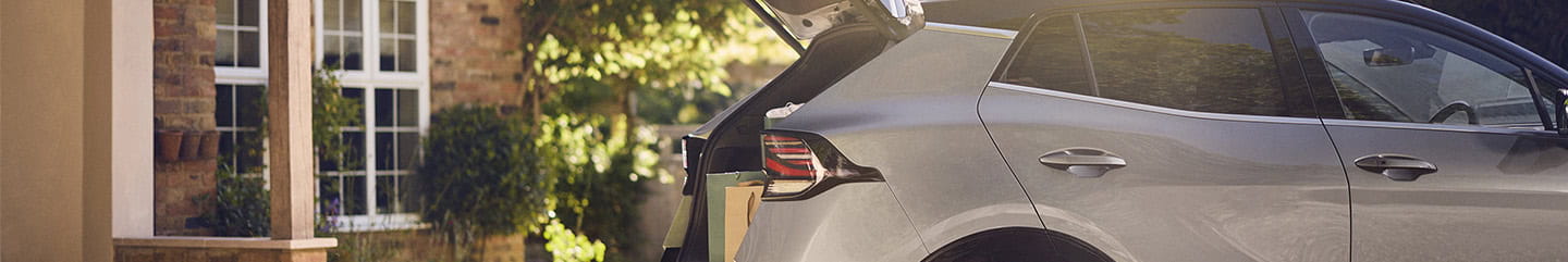 A silver and black car parked on a gravel driveway with the boot open