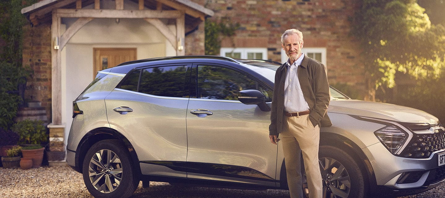 A mature man standing by his car that is parked on the drive of his family home