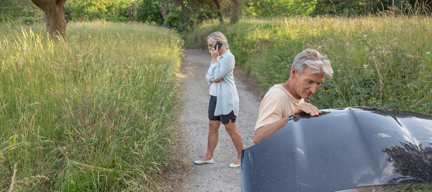 Mature woman calls for help while a mature man checks out issues with a car engine on a rural road