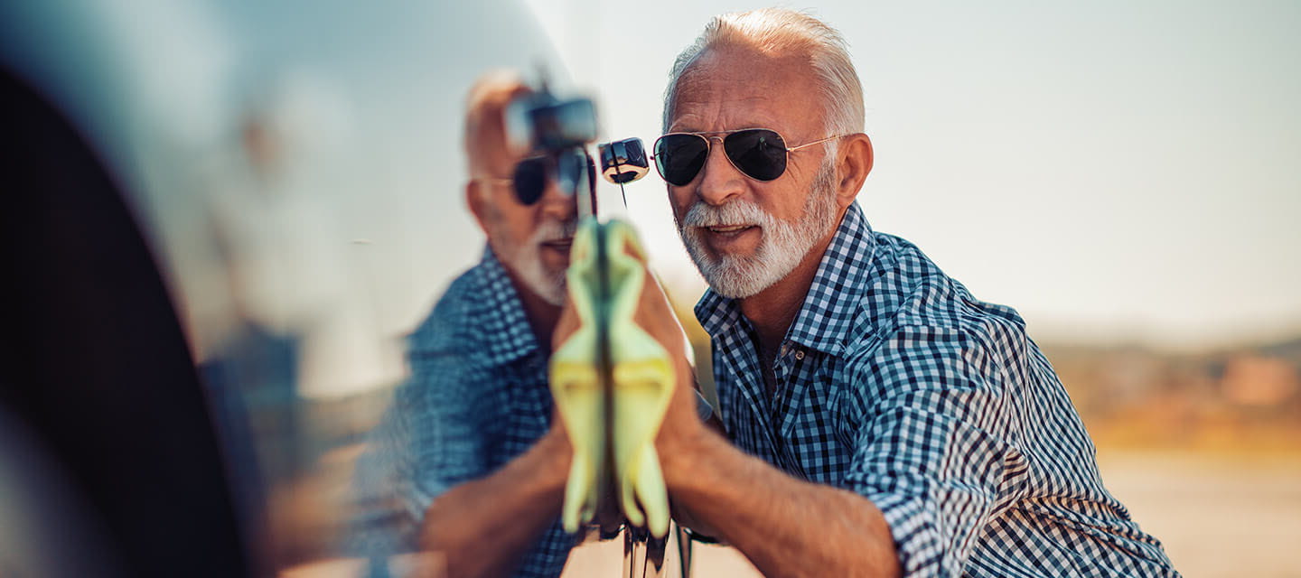 A mature man in sunglasses waxing his car