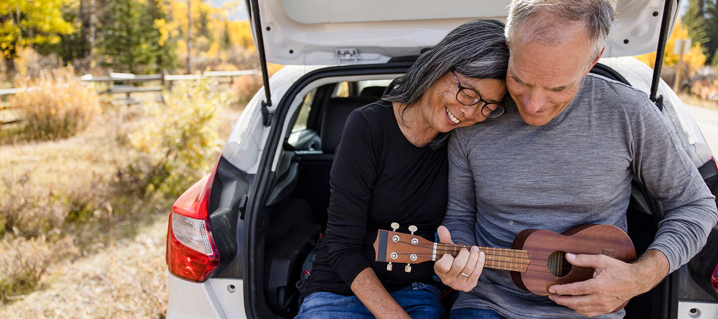 Happy, affectionate senior couple playing ukulele at back of car