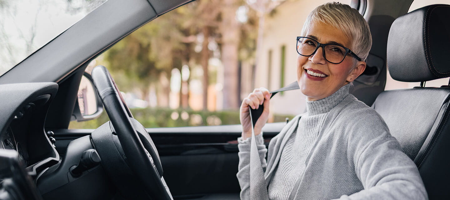 A stylish woman smiling while putting her car seatbelt on