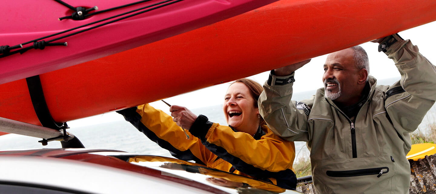 Mature couple securing kayaks to car