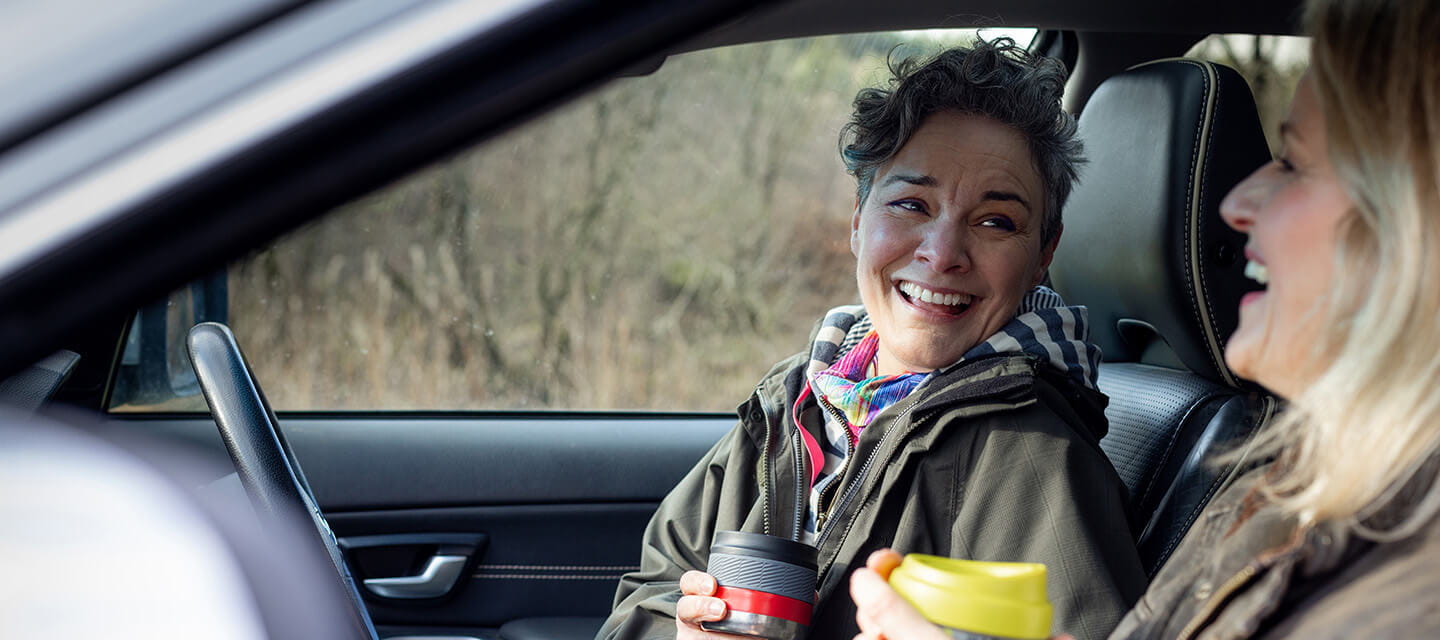 Two women sitting in a car talking and laughing together after a walk.