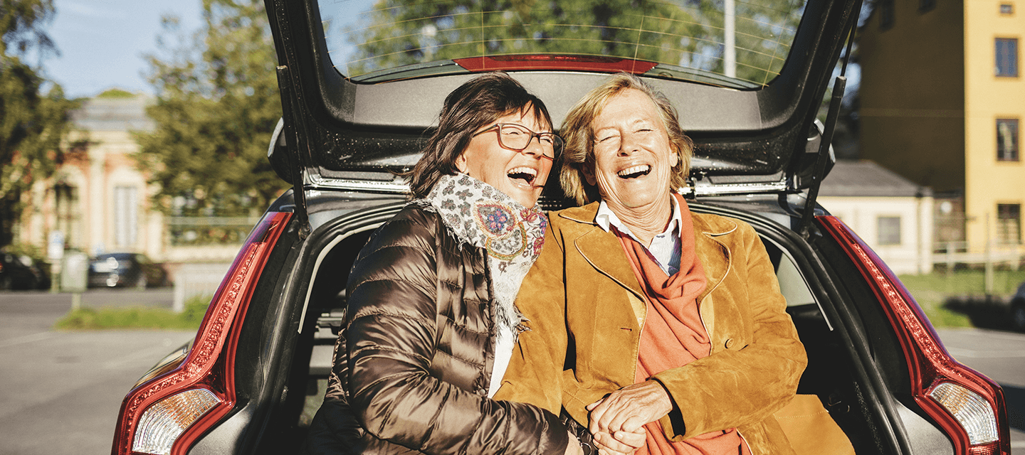 Two ladies sitting on the edge of a car boot laughing