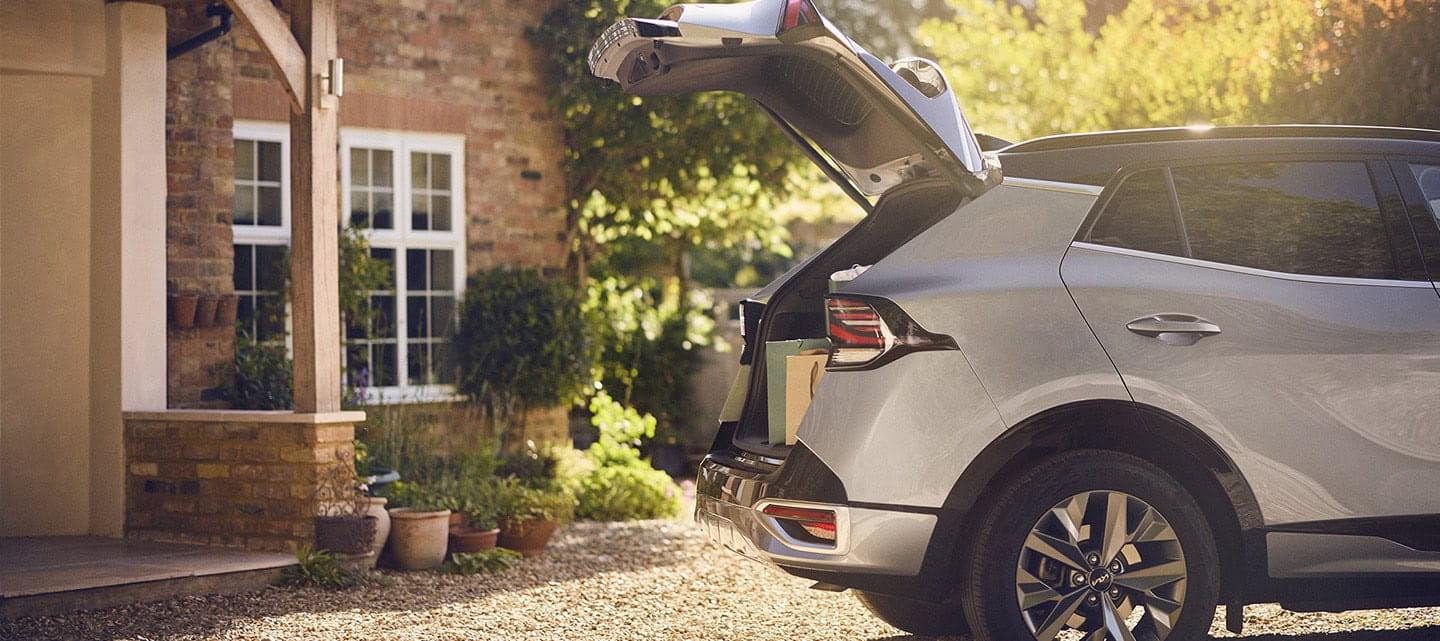 A silver and black car parked on a gravel driveway with the boot open