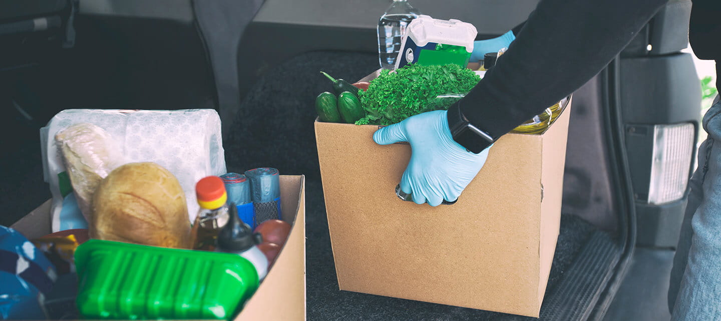 A volunteer removing a box of groceries from the back of a large car