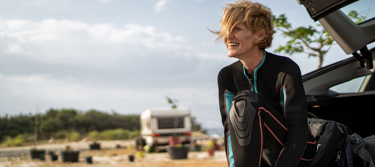 Mature female surfer getting dressed in shoes and wetsuit before going surfing