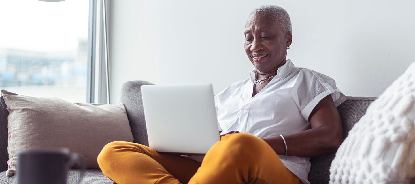 Senior business woman working from home sat crossed legged on a sofa with a laptop