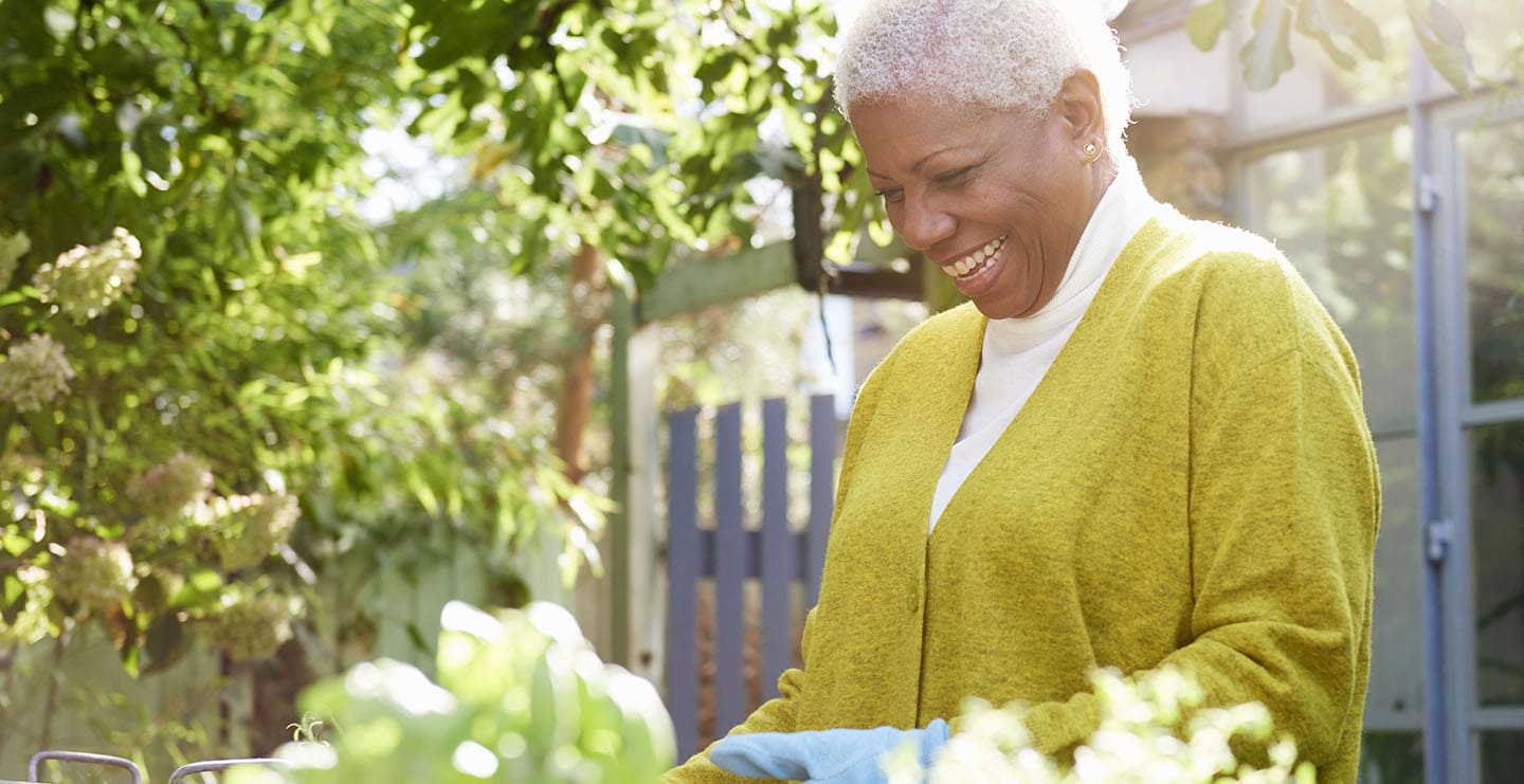 A smiling mature woman tending to plants in her garden