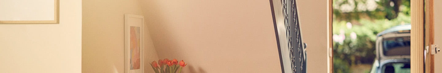 An empty hallway in a modern home, the door is ajar showing a car parked on the driveway with it's boot open.