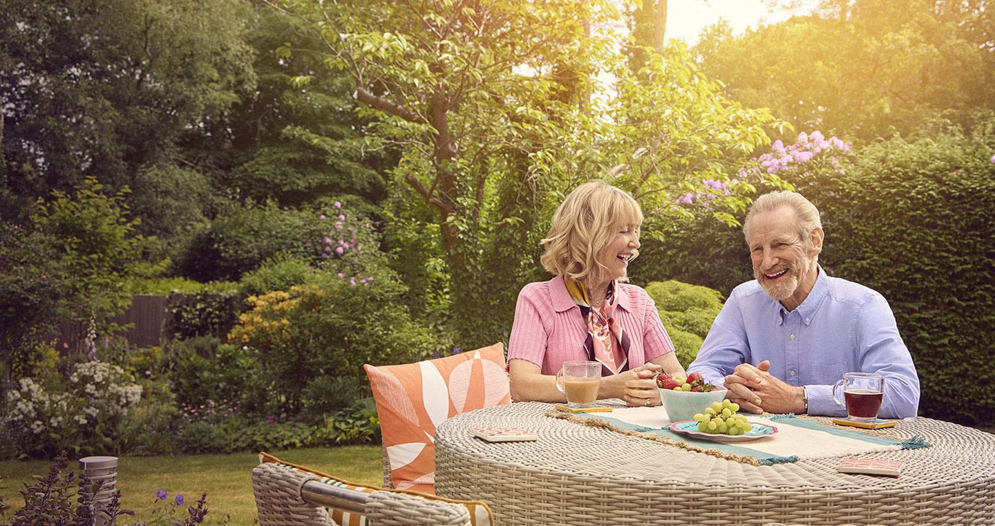 A mature couple laughing while sitting at their garden table on a sunny afternoon