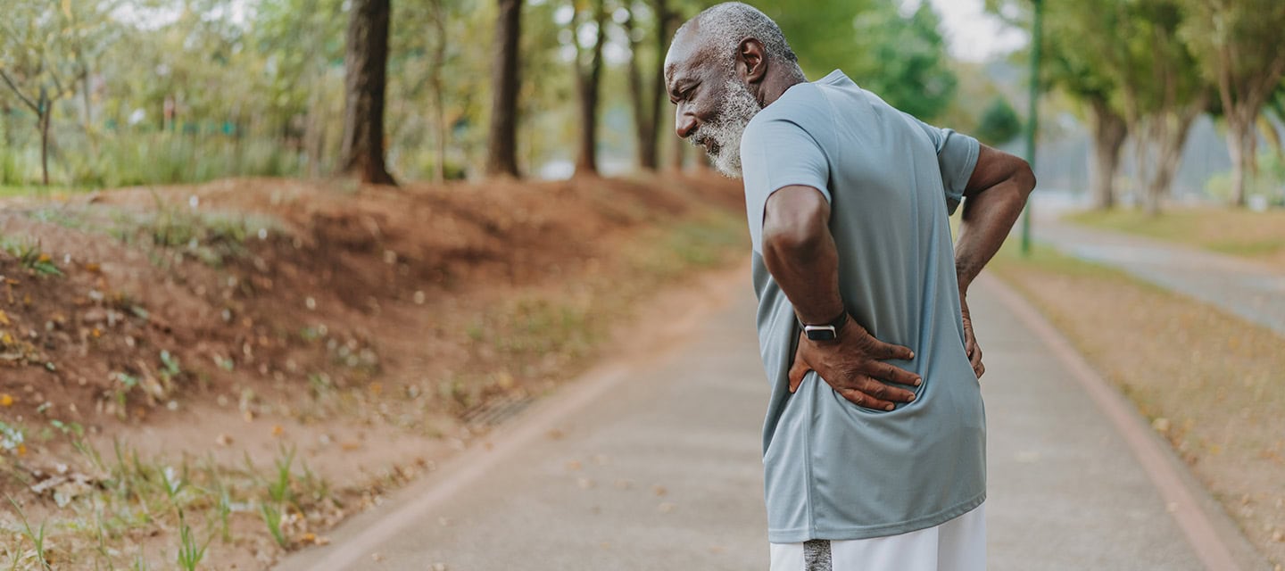 A mature man holding his back while out for exercise