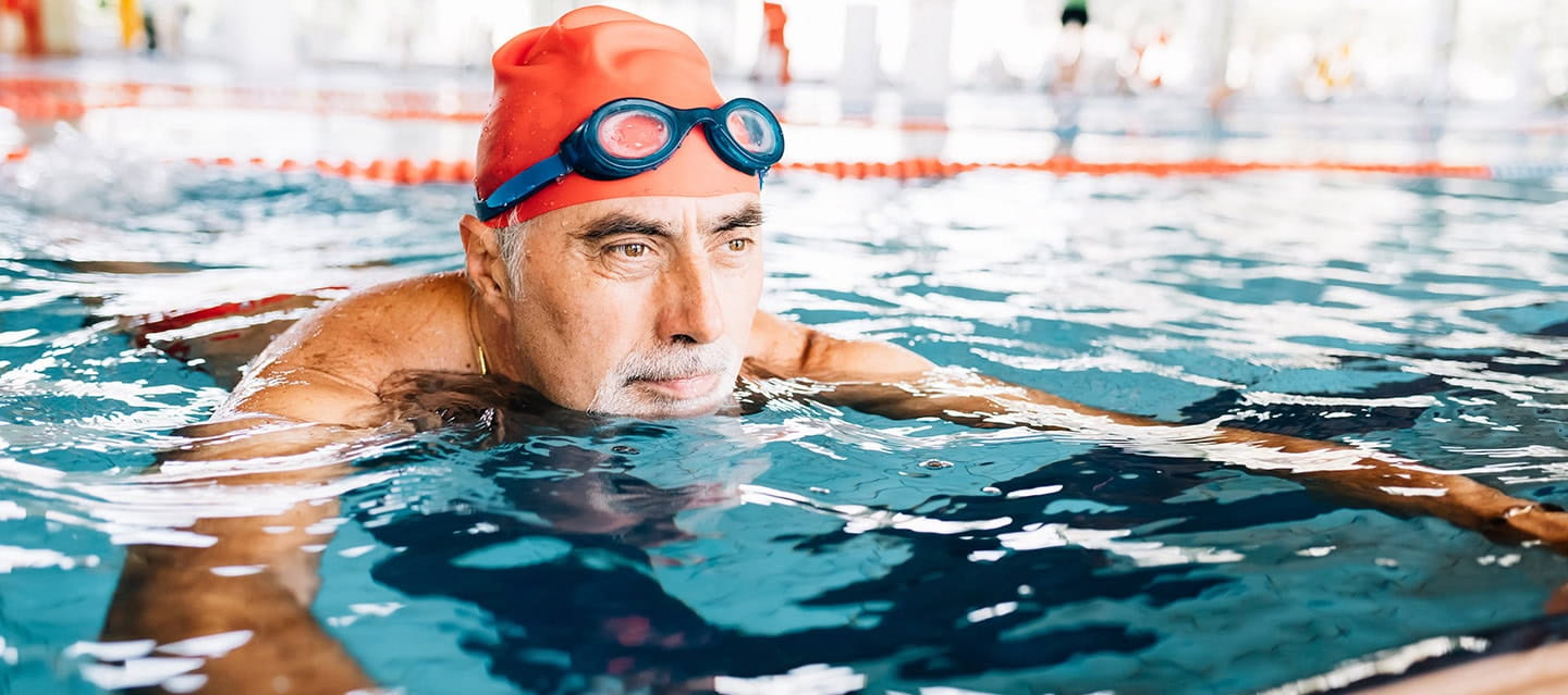 Mature man swimming at his local pool, wearing a swim hat and goggles.