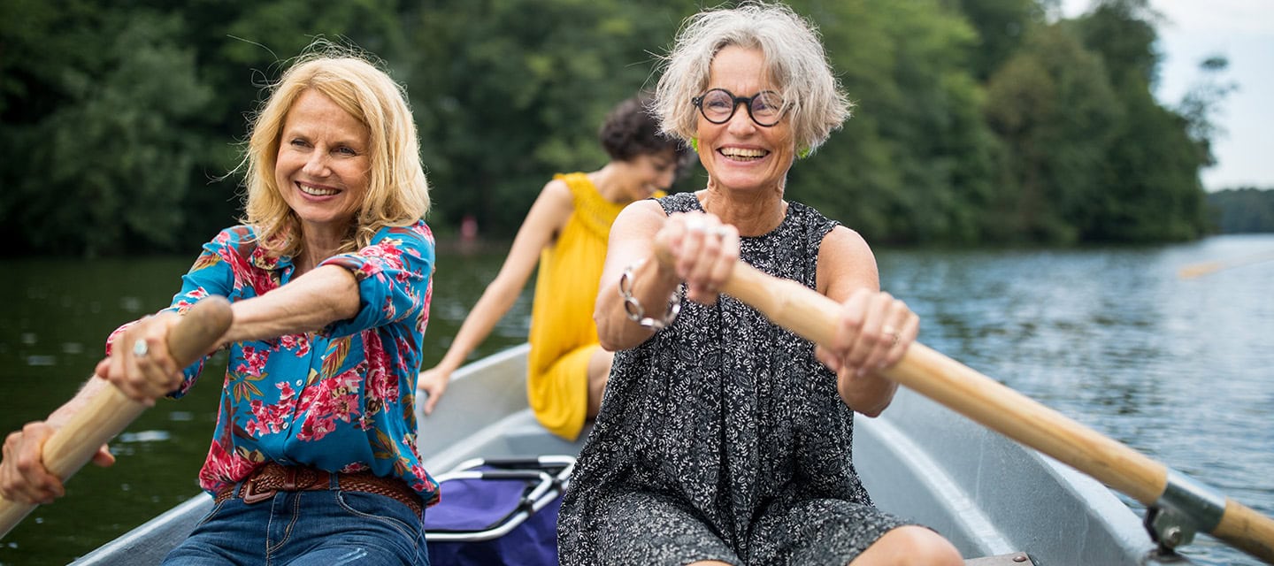 Two mature women having a terrific time rowing a boat on a lake.