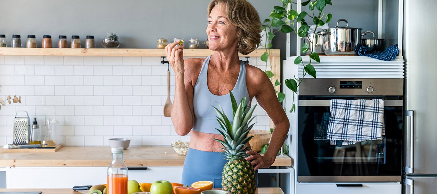 Mature woman at home wearing sportswear eating healthy food after fitness workout