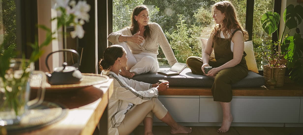Smiling female friends talking together by a window during a wellness retreat