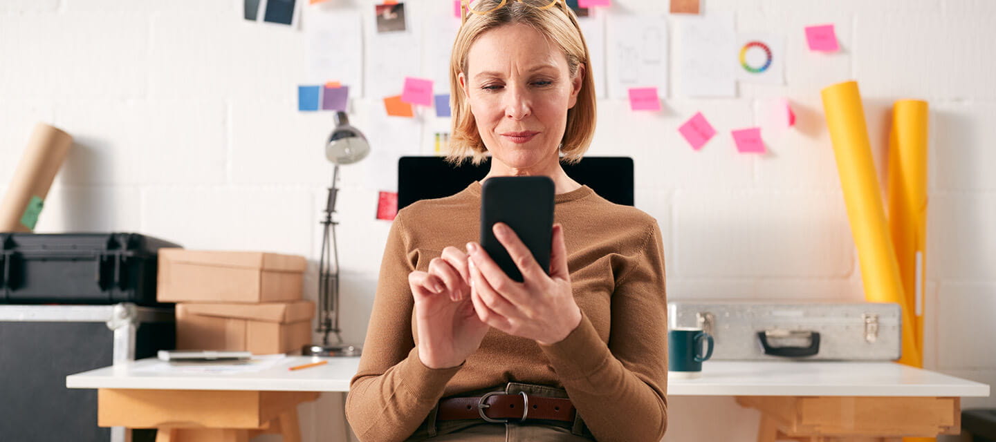 Mature businesswoman with mobile phone working at desk in start up creative business