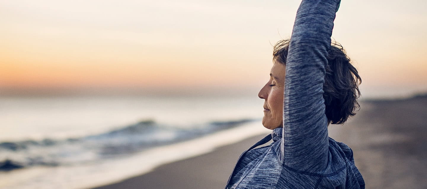 An active woman stood stretching on a sandy beach and the sun sets