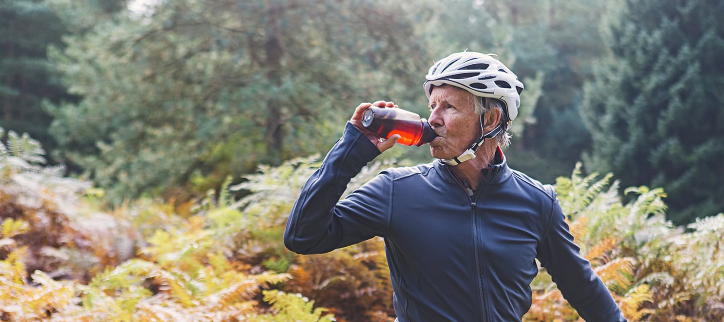 A mature cyclist taking a drinks break in an autumnal forest