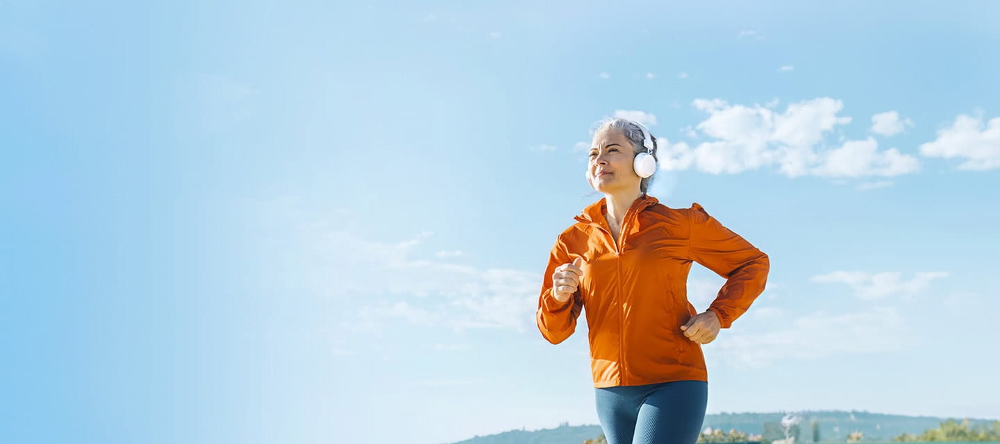 Mature woman listening to music through headphones and jogging on sunny day