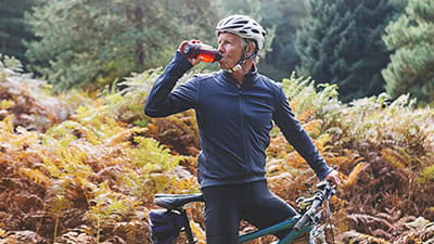 A mature cyclist taking a drinks break in an autumnal forest