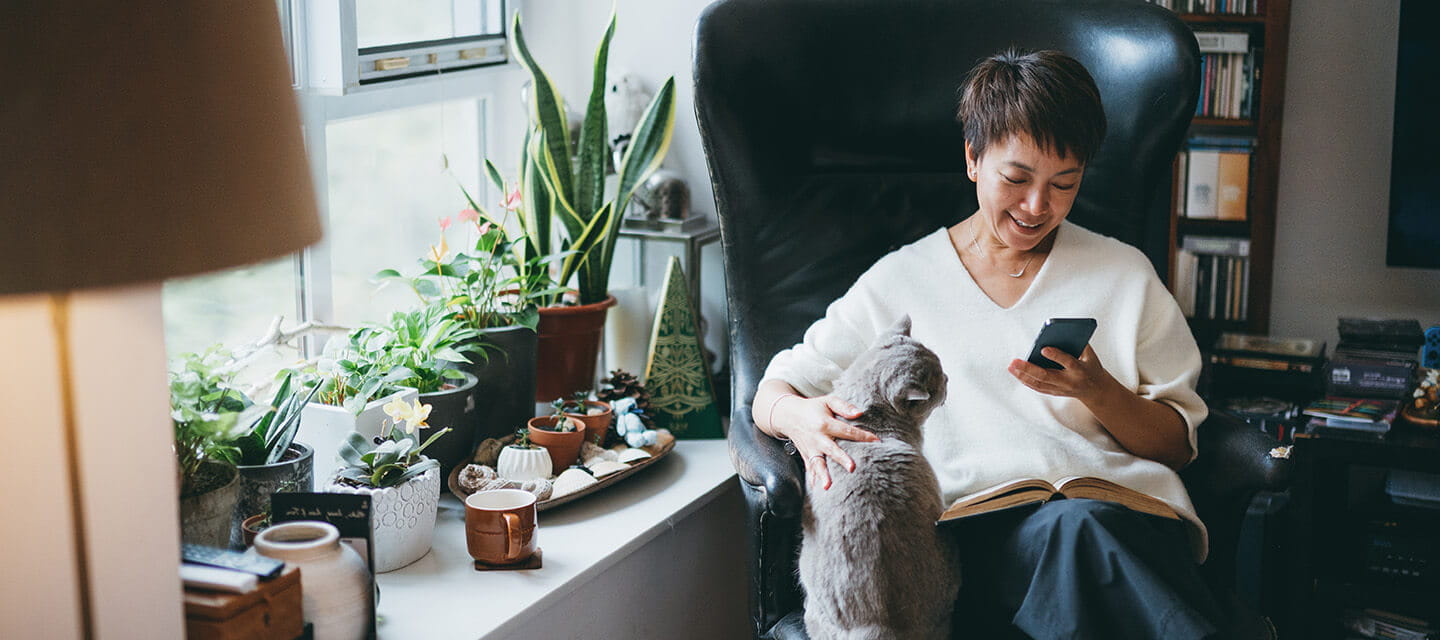 Senior woman using her smartphone at home while stroking her cat