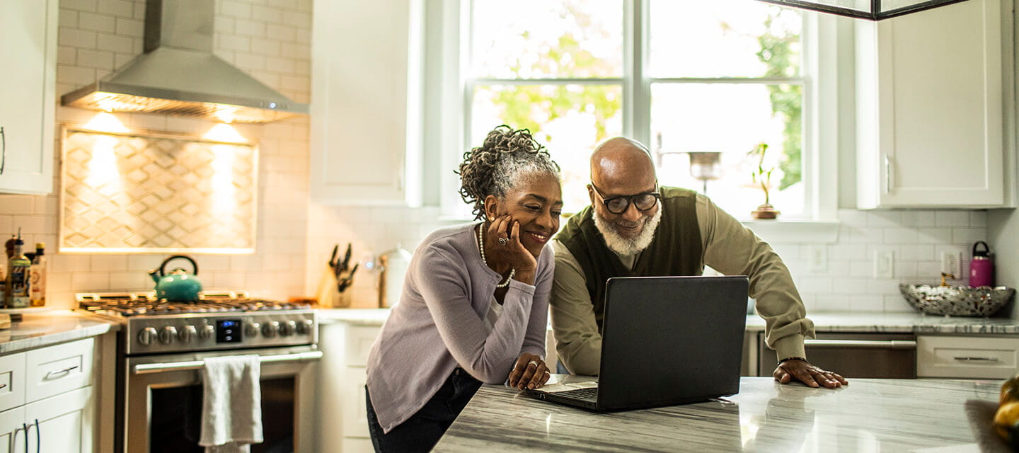 Senior couple using laptop in kitchen of suburban home