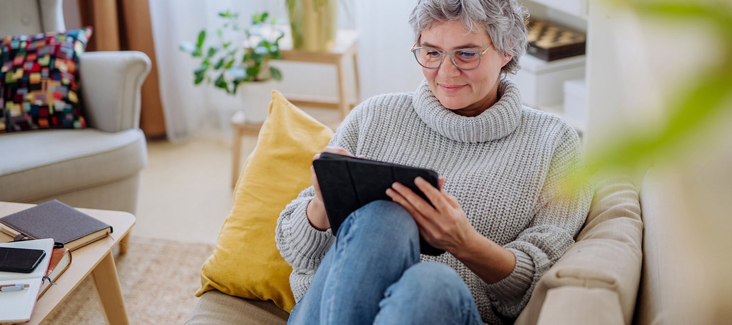 Mature woman using digital tablet while sitting on sofa at home