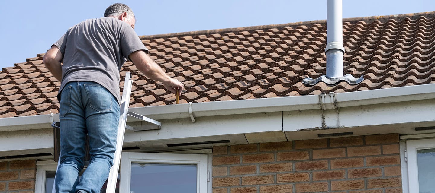 Senior man cleaning gutters on a suburban English house.