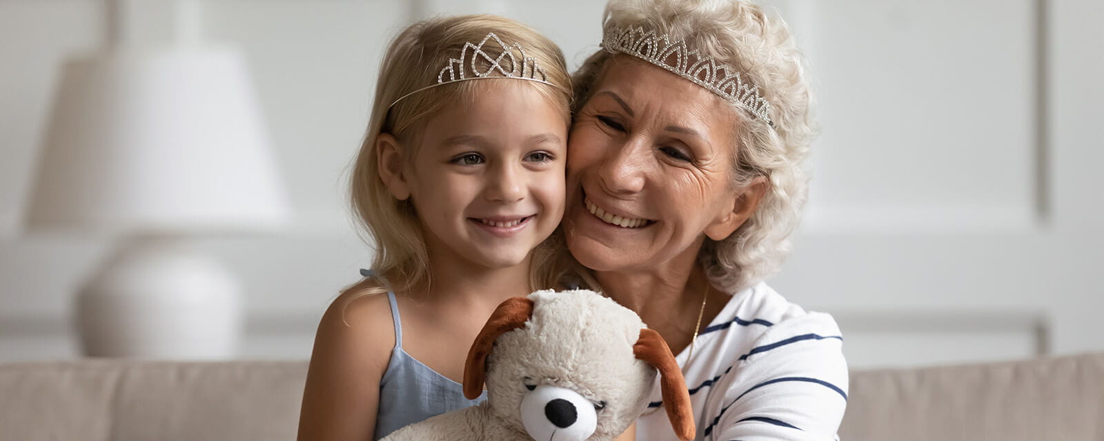 A grandmother and granddaughter in a happy embrace while wearing tiaras