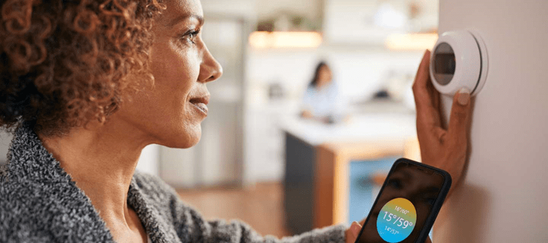 A woman adjusting her thermostat and looking at the app on her smartphone